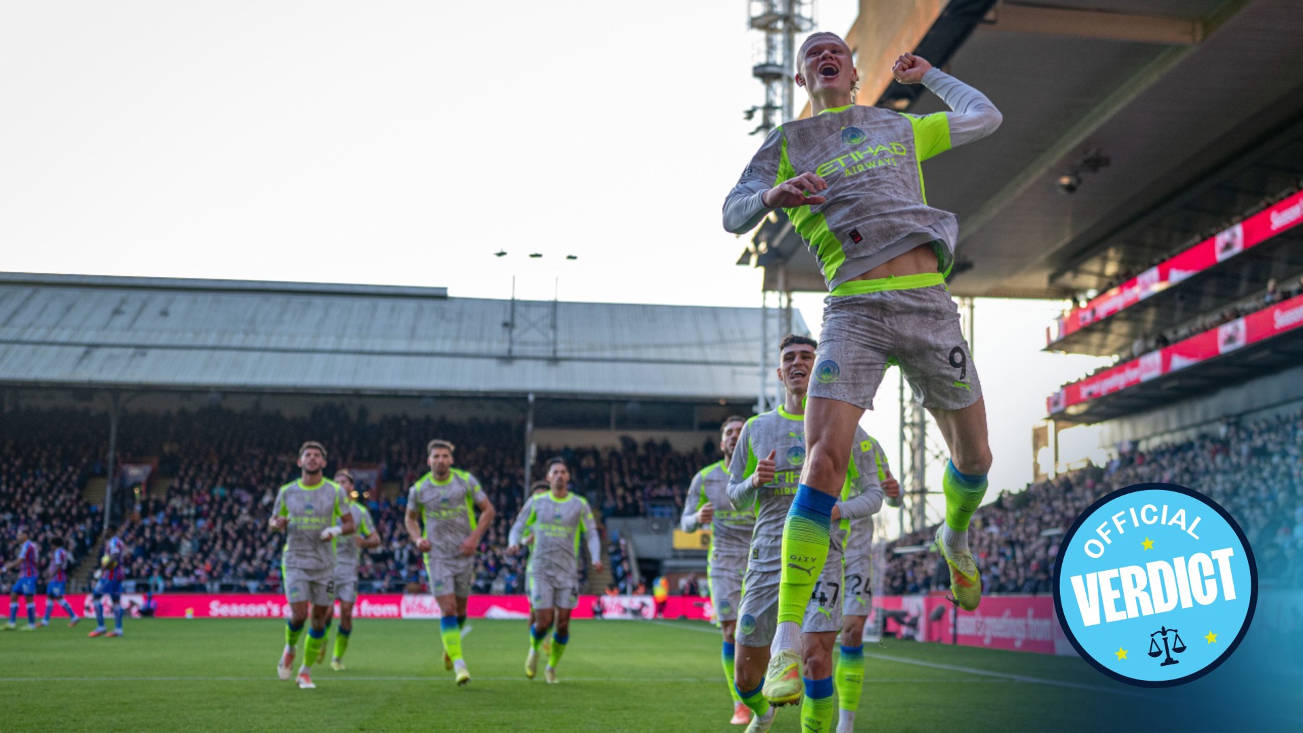 A Manchester City player jumps in celebration after scoring a goal, while teammates follow behind wearing gray and neon kits. 'Official Verdict' text is visible in the corner.