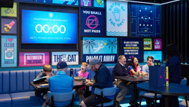 A lively restaurant with soccer-themed decorations and a countdown screen showing 00:00 for a match. People are seated in booths, enjoying food and beverages.