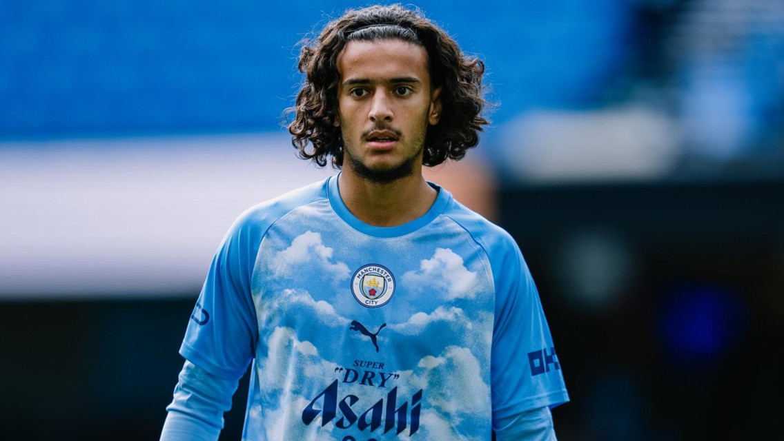 A Manchester City player wearing an Asahi Super Dry jersey with a sky and cloud design.