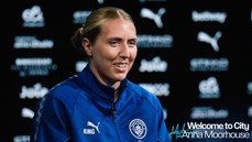 A person in a blue Manchester City sports jacket, with the text 'Welcome to City Anna Moorhouse' visible. Background is filled with Manchester City-related logos.