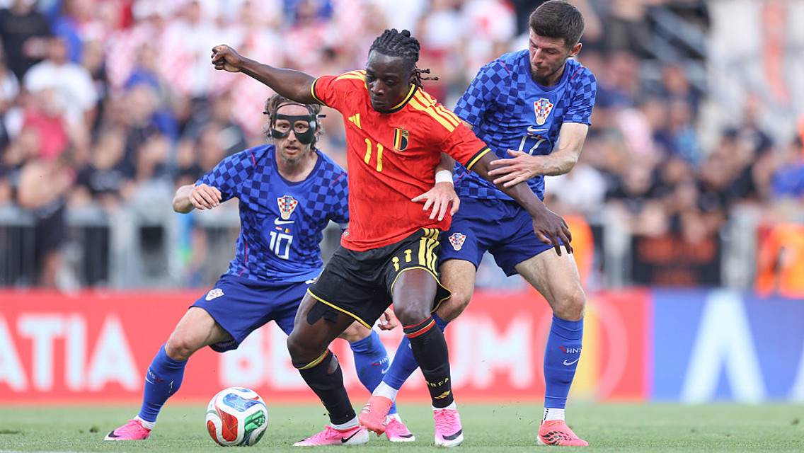 Soccer match where a player in a red Belgium jersey is trying to get past two players in blue Croatia jerseys.