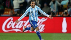 A soccer player in an Argentina jersey with the number 11 celebrates with arms spread wide on the field. A Coca-Cola advertisement is visible in the background.