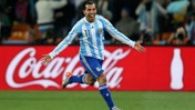 A soccer player in an Argentina jersey with the number 11 celebrates with arms spread wide on the field. A Coca-Cola advertisement is visible in the background.