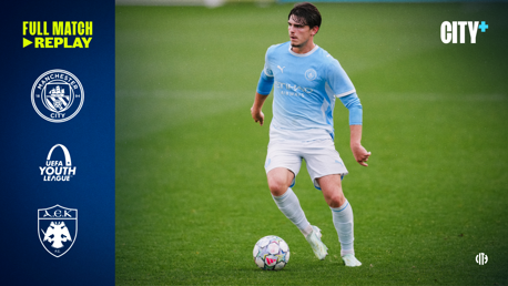 Male football player in Manchester City kit during UEFA Youth League match. Logos of Manchester City and AEK. Text reads 'Full Match Replay' and 'City+'.