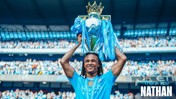 A footballer wearing a blue Manchester City shirt lifts the Premier League trophy over their head. The stadium is filled with fans, and the text 'Thank You Nathan' is visible in the image.
