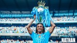 A footballer wearing a blue Manchester City shirt lifts the Premier League trophy over their head. The stadium is filled with fans, and the text 'Thank You Nathan' is visible in the image.
