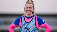 A football player wearing a blue and pink training kit with a Puma branded bib on a field.