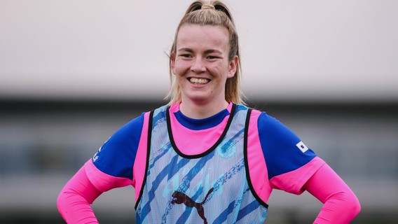 A football player wearing a blue and pink training kit with a Puma branded bib on a field.