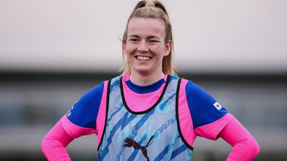 A football player wearing a blue and pink training kit with a Puma branded bib on a field.