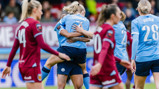 Football players celebrating a goal on the field. A player in a sky blue jersey with 'Coombs' on the back is being hugged by a teammate.