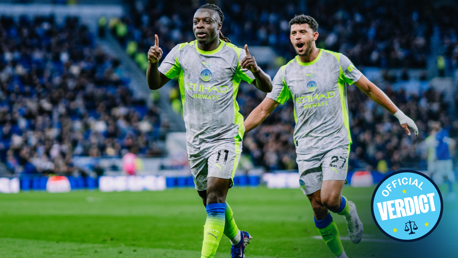 Two Manchester City players in white and neon green kits celebrate on the field with blurred faces. The image includes 'Official Verdict' text in a circle.