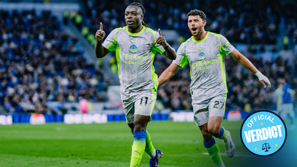Two Manchester City players in white and neon green kits celebrate on the field with blurred faces. The image includes 'Official Verdict' text in a circle.