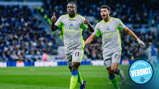 Two Manchester City players in white and neon green kits celebrate on the field with blurred faces. The image includes 'Official Verdict' text in a circle.