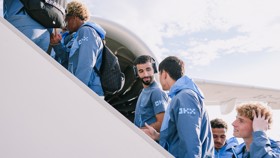Group of people in matching blue jackets boarding an airplane. They carry backpacks and engage in conversation as they ascend the stairs.