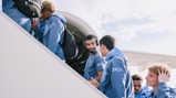 Group of people in matching blue jackets boarding an airplane. They carry backpacks and engage in conversation as they ascend the stairs.
