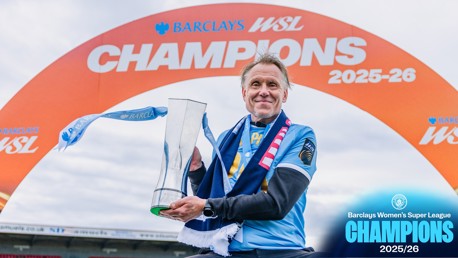 A person holding a trophy in front of a Barclays WSL Champions 2025-26 sign.