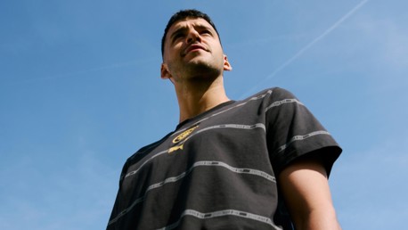 A man in a black shirt with a striped pattern and logo, looking upwards against a clear blue sky.