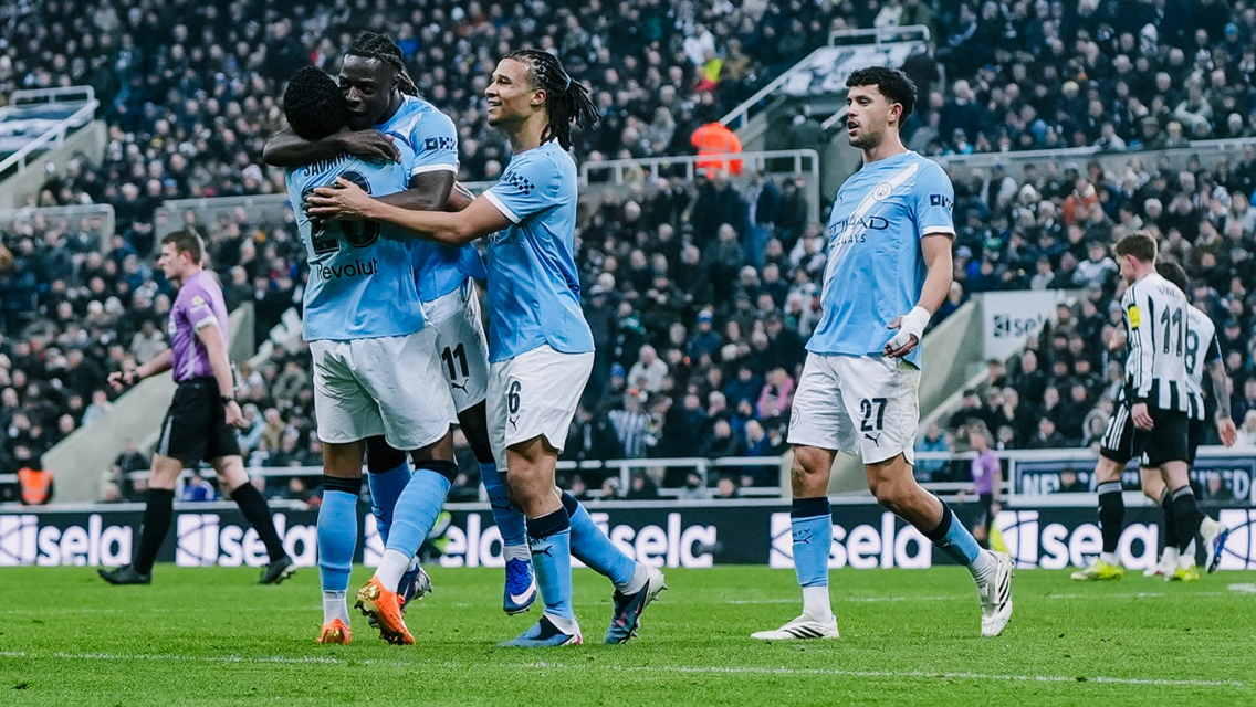 Manchester City players celebrating a goal in a football match against Newcastle United with a crowded stadium in the background.