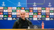 A bald individual speaks at a UEFA Champions League press conference with sponsor logos displayed in the background.