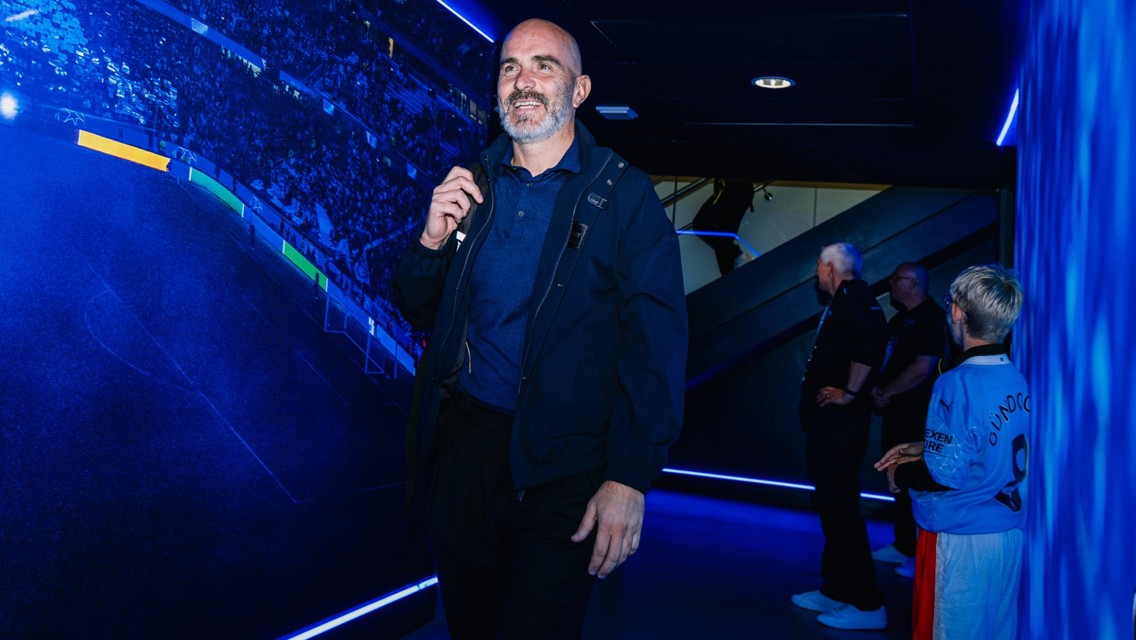 A man wearing a blue jacket walking through a blue-lit tunnel. A child in a blue sports jersey stands nearby.