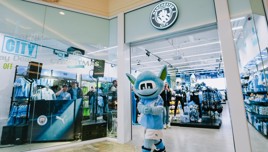 Manchester City's mascot stands outside the club store, surrounded by team merchandise and decorations promoting Christmas deals.