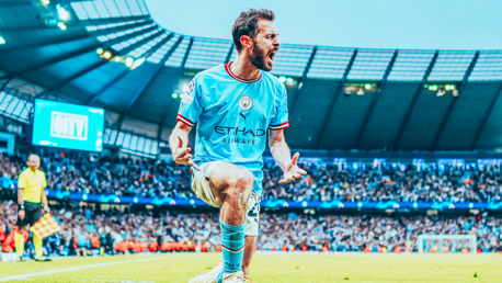 A Manchester City player celebrates a goal at the Etihad Stadium, wearing the team's sky blue kit sponsored by Etihad Airways, with a large crowd visible in the background.