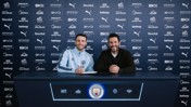 Two individuals at a contract signing table with Manchester City branding in the background.