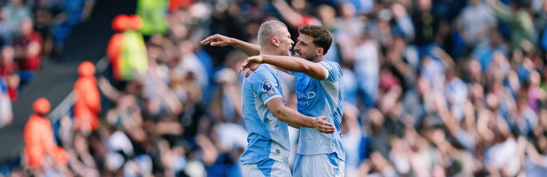 Two Manchester City players hugging on the field during a goal celebration.