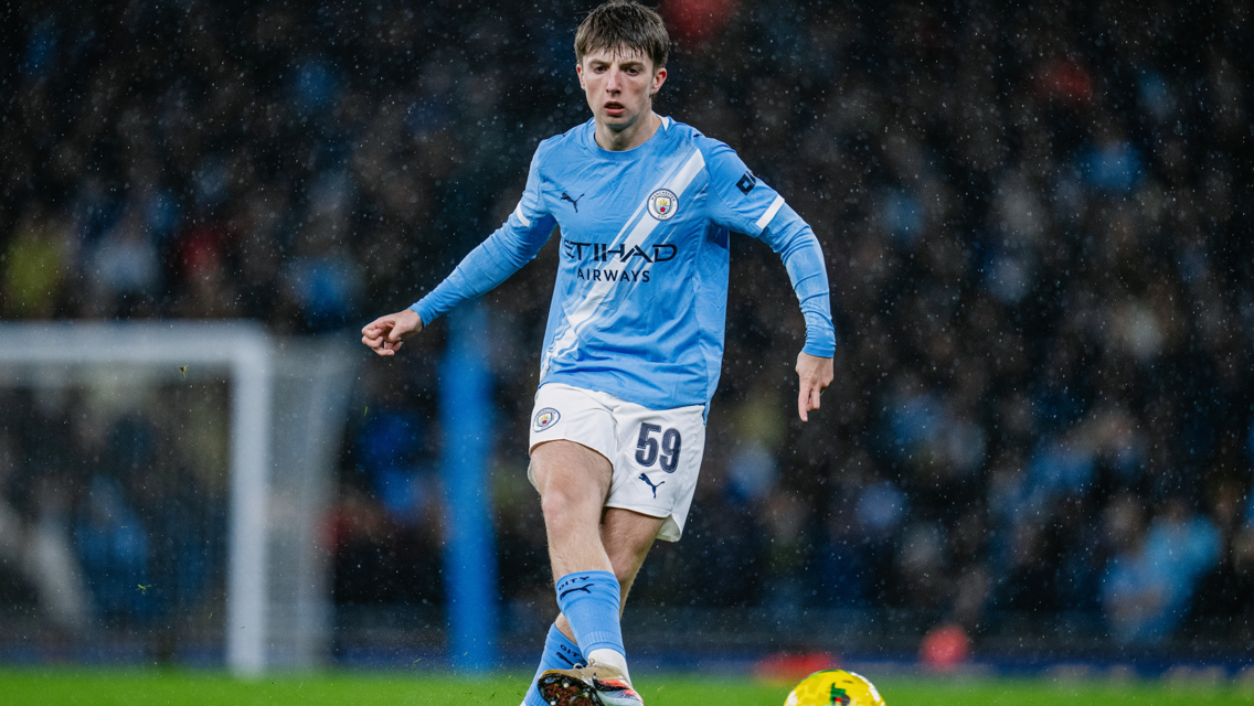A football player wearing the Manchester City kit with number 59, playing on a rain-soaked field.