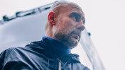A person wearing a black jacket looks up with the sky in the background.