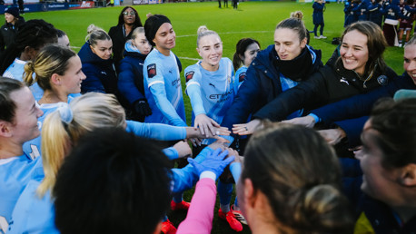 A huddle of Manchester City Women's football team wearing light blue jerseys on the field.