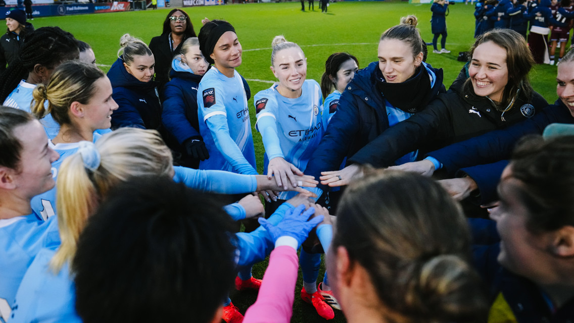 A huddle of Manchester City Women's football team wearing light blue jerseys on the field.