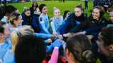 A huddle of Manchester City Women's football team wearing light blue jerseys on the field.