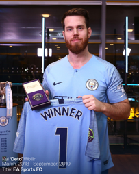 A person holding a Manchester City jersey labeled 'Winner' and a Premier League award. The background shows trophies and a list of League Cup victories.
