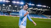 Football player in Manchester City kit celebrating on the pitch with a blurred face.