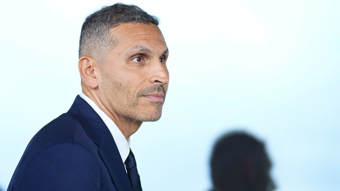 A man in a suit looking sideways against a blue background.