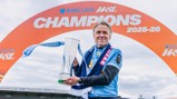 Person holding a trophy under an arch labeled 'BARCLAYS WSL CHAMPIONS 2025-26'.