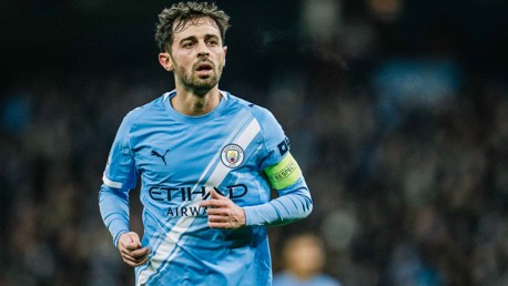 A football player in a Manchester City kit with sponsor logos during a match, wearing a captain's armband.