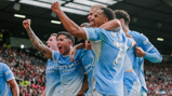 Group of football players in Manchester City jerseys celebrating a goal during a match.
