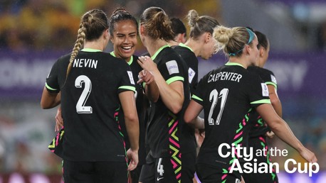 Soccer team huddle during the Asian Cup match, with players numbered 2 and 21 visible, wearing black kits with green accents.