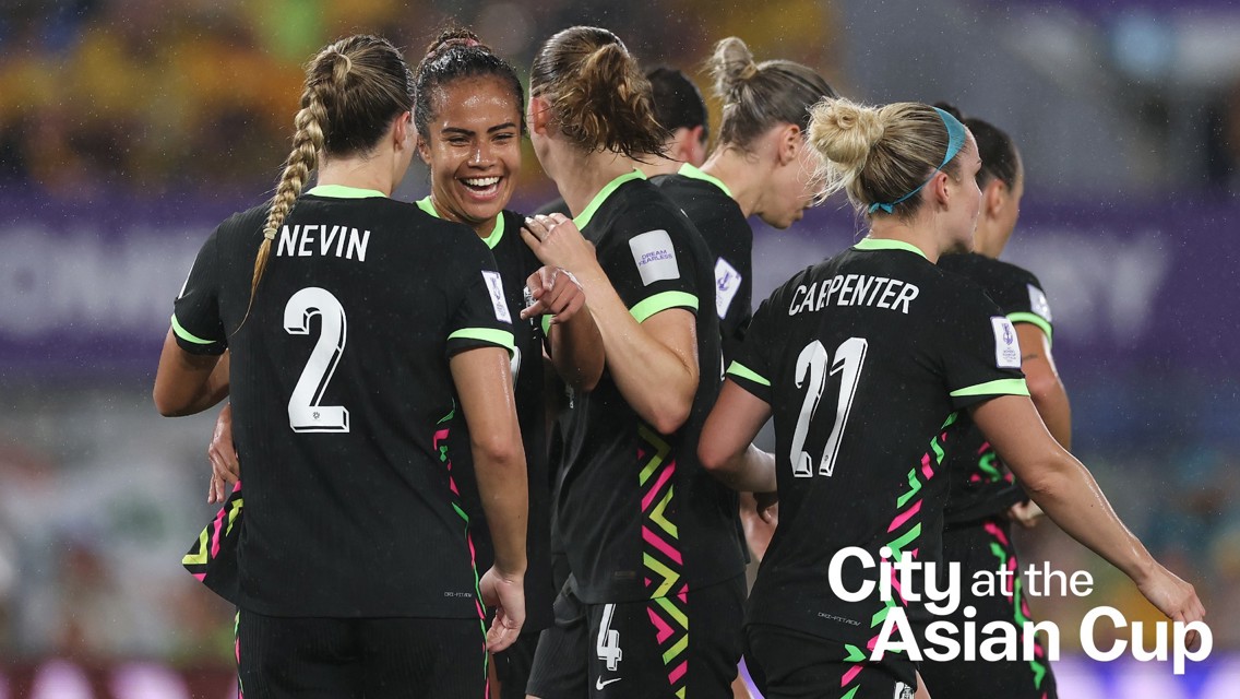 Soccer team huddle during the Asian Cup match, with players numbered 2 and 21 visible, wearing black kits with green accents.
