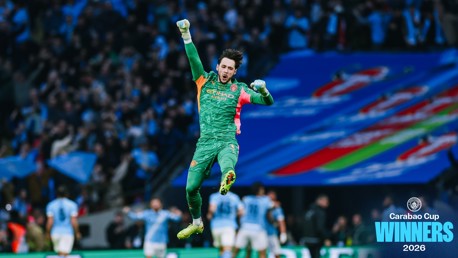 A football player in a green kit jumps in celebration with 'Carabao Cup Winners 2026' text and Manchester City logo in the corner.