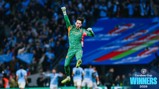 A football player in a green kit jumps in celebration with 'Carabao Cup Winners 2026' text and Manchester City logo in the corner.