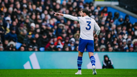 A soccer player wearing a white jersey with blue shorts and blue-striped socks. The jersey has the name 'Ruben' and number '3' on the back. The player is pointing, and the background shows a crowd in stadium seating.