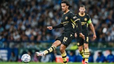 A football player in a black and yellow Manchester City kit, marked with number 32, poised to kick a ball during a match.