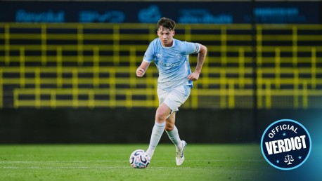 A young soccer player from Manchester City in a light blue kit dribbles the ball on the field with a badge reading 'Official Verdict' in the lower right corner.
