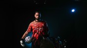 A soccer player wearing the Manchester City goalkeeper kit, holding a soccer ball, with Etihad Airways logo visible, in a dimly lit setting.