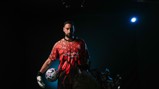 A soccer player wearing the Manchester City goalkeeper kit, holding a soccer ball, with Etihad Airways logo visible, in a dimly lit setting.