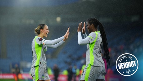 Two female soccer players in green and gray jerseys high-fiving on a rainy field. One wears '9' with the name 'BORN' on her back. An 'Official Verdict' stamp is in the bottom right corner.