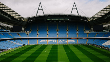 View of the football pitch inside Etihad Stadium with blue seating and Etihad branding visible.